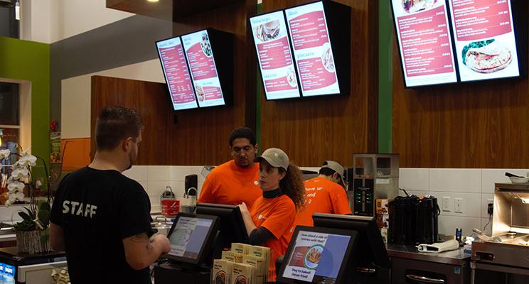 An employee takes the order of a customer at a quick service restaurant with NexSigns digital menu boards