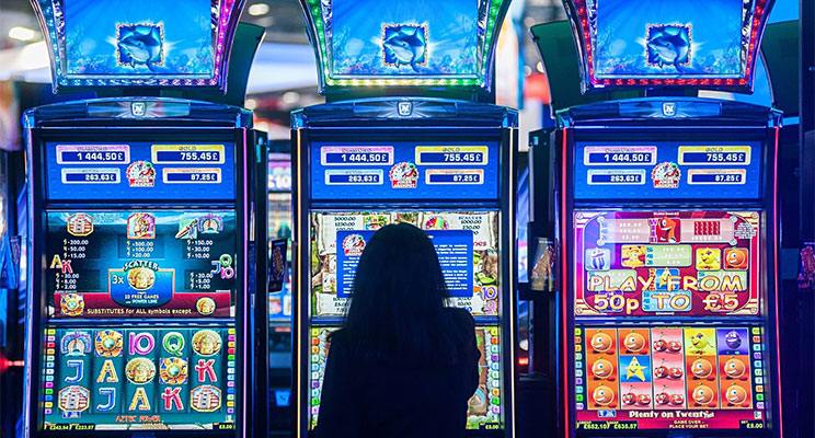 Woman sitting at a slot machine with the machine backlighting with its vibrant digital displays